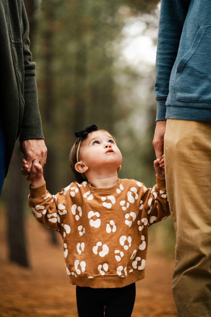 a little boy looking up while holding hands with two adults